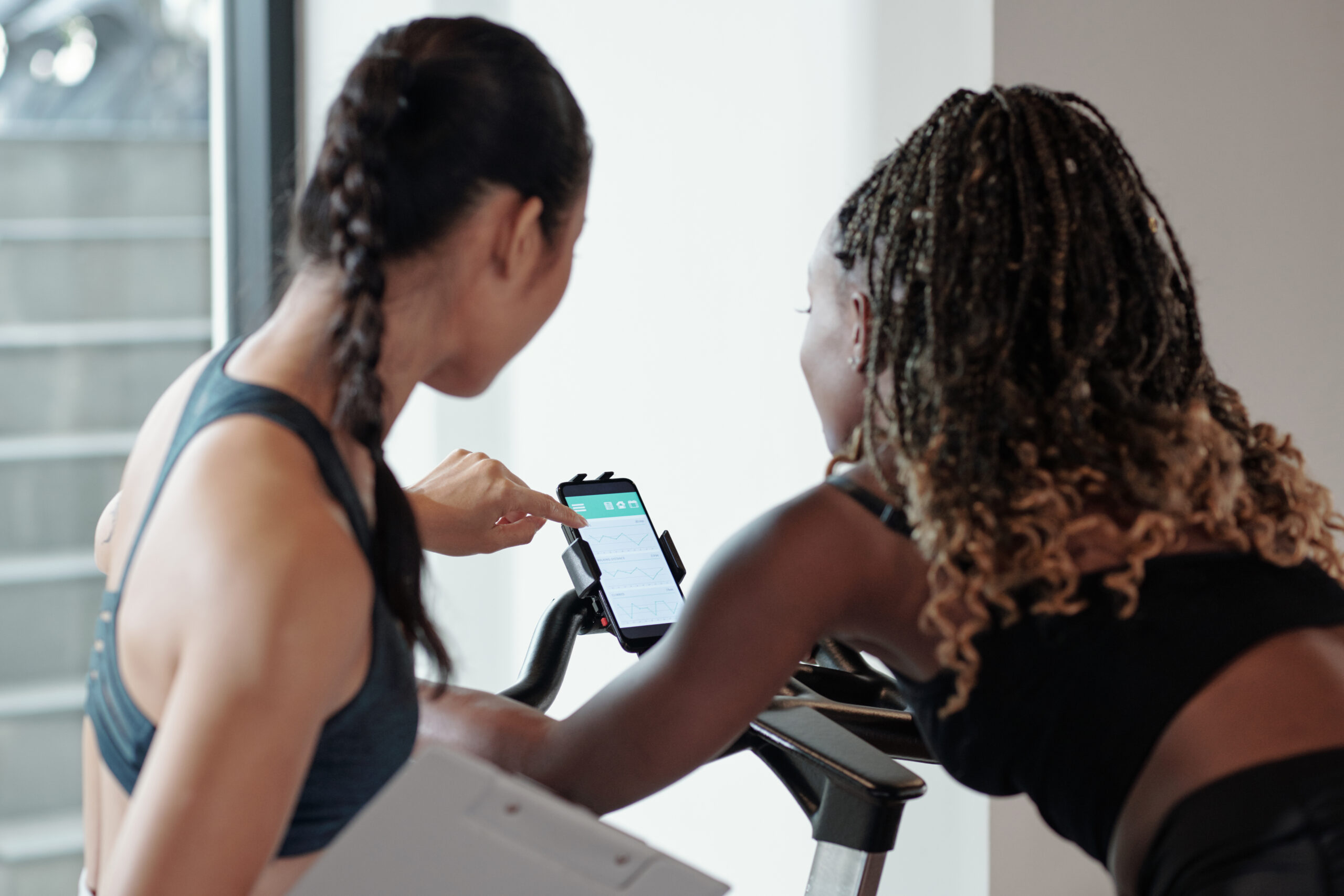 Fitness trainer checking heart rate of female client via application on smartphone